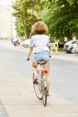 Rear view of young woman wearing casual clothes while riding on his bicycle on a warm summers's day