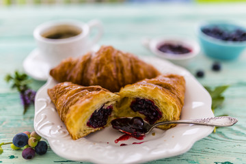 Croissant with blueberries on white plate on wooden table in the garden