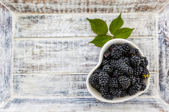 Fresh blackberries in bowl on wooden background with space for text
