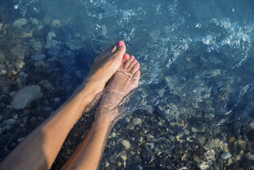 Young and beautiful female feet with red painted nails on a beach under waves.