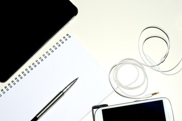 Vista dall'alto di un notes e penna e un cellulare e un tablet, sulla scrivania bianca