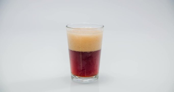 A glass with a red drink and some bubbles is standing in a cup. We can see how the foam is slowly disappearing. Close-up shot.
