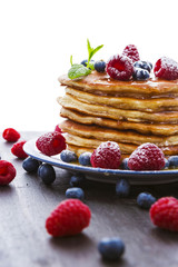 Pancakes with honey and berries on white background
