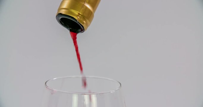 Someone is pouring red wine into a glass that is standing on a table in the kitchen. There is not much wine left in the bottle and he empties it completely. Close-up shot.
