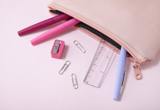 A school pencil pouch with pens spilling out on to a pastel pink background