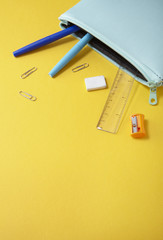 A pale blue pencil case with pens spilling out on to a yellow background, forming a page border