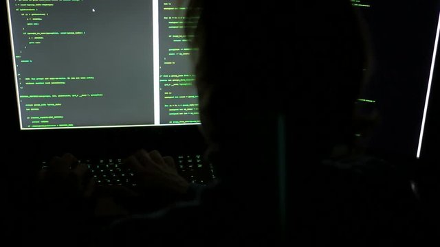 A hacker is typing code on multiple screens in darkness	A hacker is typing code on multiple screens in darkness. Maybe he is a cyber-criminal hacking in to steal your money!