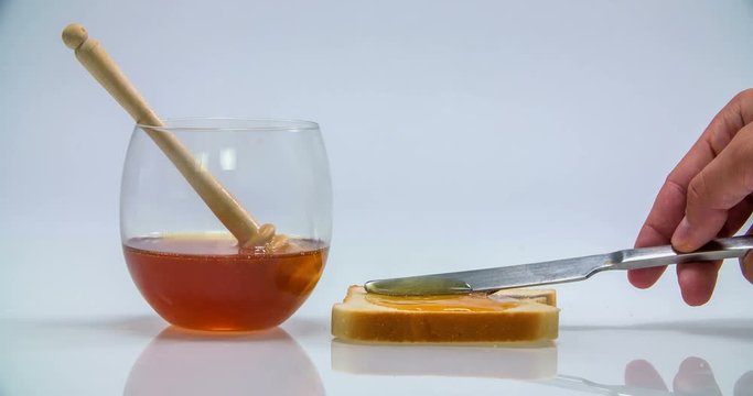 Someone is spreading out honey on a piece of toast and then when he is removing the knife, he is leaving some drops of honey on the kitchen counter.
