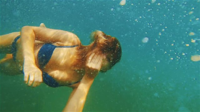 Girl in a bathing suit dives into the sea with a closed nose. She looks at the camera with eyes open. Underwater shooting.