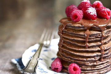 Stack of chocolate pancakes topped with chocolate and fresh rasp