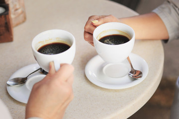 Women's hands are holding white cups with coffee.