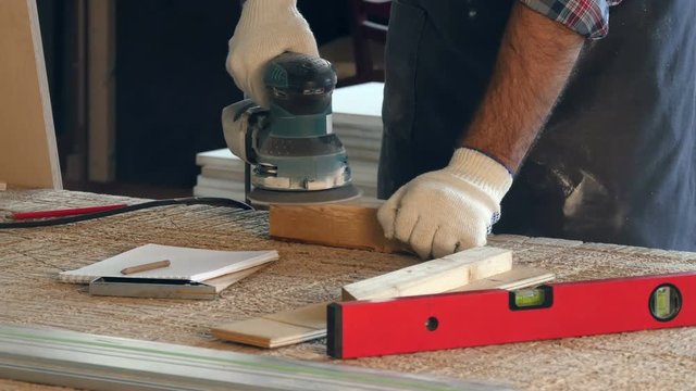 Man working with wooden planck and electric planer in workshop.
