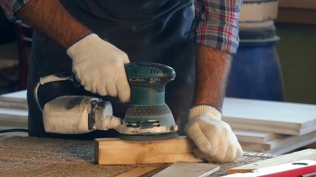The zarpenter working with electric planer on wooden plank in workshop.Hands.