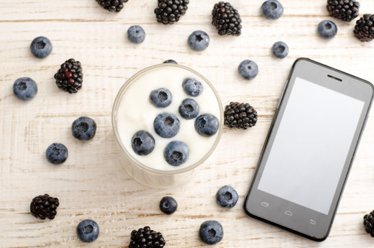 Top view of a yogurt with blueberries, smartphone, berries on the table
