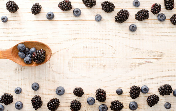 Framing of blackberry and blueberry fruit in a wooden spoon on a light wooden table