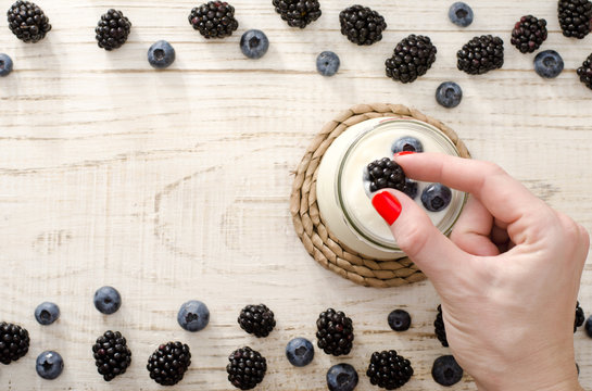 Blackberries in a female hand, yogurt with blueberries, on the edge of the berries, light background