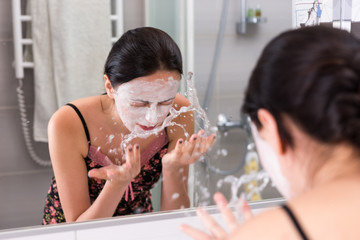 Woman with cosmetic mask spraying water on her face standing in