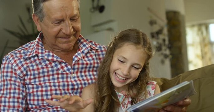 Cute girl sitting in the lap of their grandfather and looking happily together at a photo album