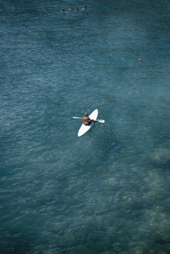 Man on surfboard paddling in the crystal clear sea