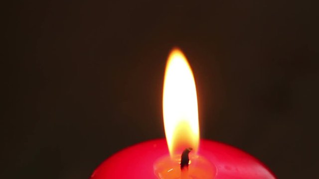 Burning candle in red wax on a dark background.