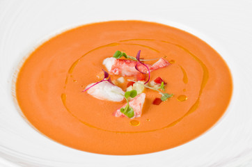 Pumpkin cream soup with cucumbers, tomatoes, shrimp and olive oil on a plate on a white background, closeup