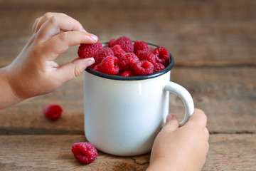 In the hands of a child juicy, fresh raspberries in a bowl