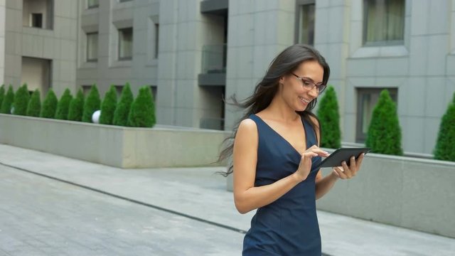 Fashionable woman using tablet pc walking outside. Modern businesswoman wearing stylish clothes and glasses