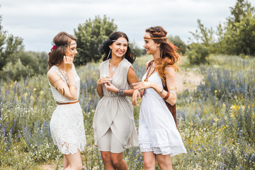 Three beautiful cheerful hippie girls, best friends, the outdoors, cute smile, trendy hairstyles, feathers in her hair, white dress, tattoo flash, gold accessories, Bohemian, boho style, fashion indie © Nabokov Alex
