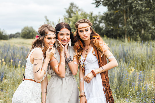 Three beautiful cheerful hippie girls, best friends, the outdoors, cute smile, trendy hairstyles, feathers in her hair, white dress, tattoo flash, gold accessories, Bohemian, boho style, fashion indie