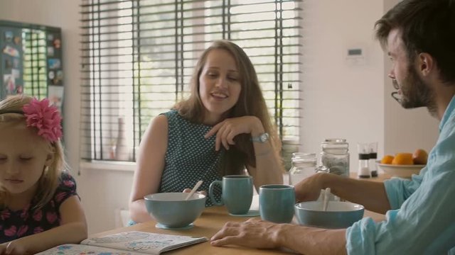 Two young parents having a conversation at the kitchen table while their daughter is colouring. Slow mo, Steadicam shot