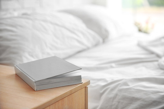 Closed Book On Wooden Bedside Table Near Crumpled Bed