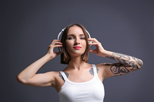 Beautiful young woman with tattoo wearing headphones and posing on gray background