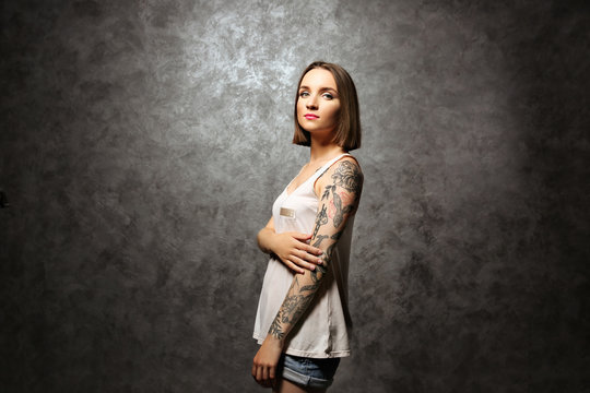 Beautiful young woman with tattoo posing on gray background