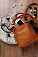 Brown leather backpack with female items on wooden surface, top view
