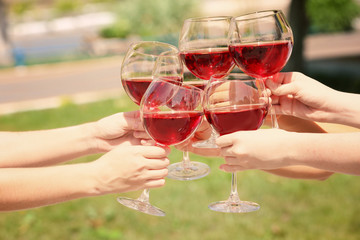 Female hands clinking glasses with red wine, outdoors