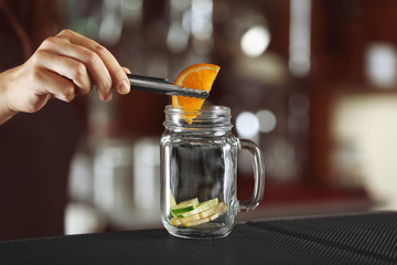 Woman hands putting fruits into glass jar on bar counter