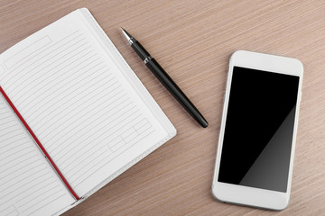 Notepad, pen and phone on wooden background