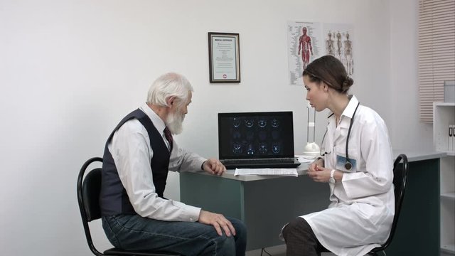Doctor showing elderly patient's mri results on laptop.
