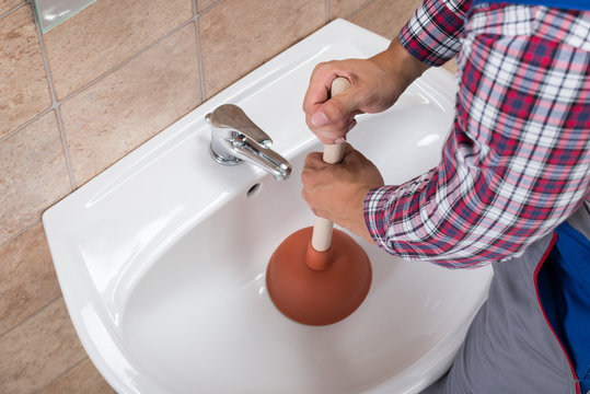 Plumber Using Plunger In Bathroom Sink