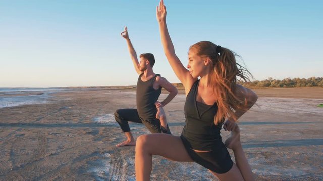 Young couple is practicing yoga on the beach at sunrise background, slow motion