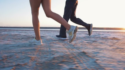 Young couple running on the beach at sunrise background, slow motion, close up - Powered by Adobe