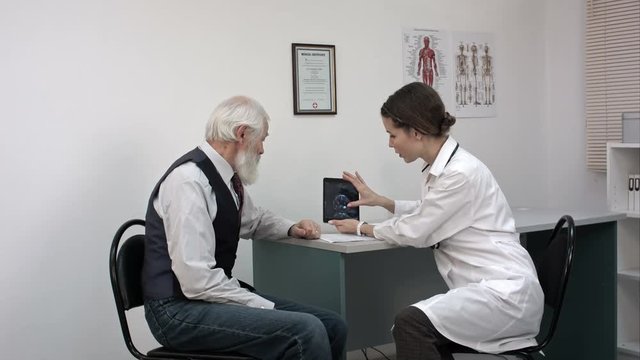 Female doctor reviewing x-ray on a tablet with mature patient.