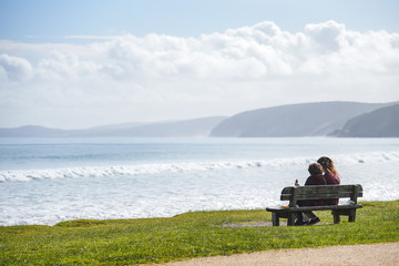 couple on wooden bench look out to sea