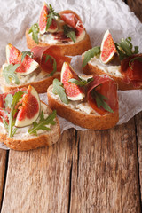Bruschetta with ripe figs, prosciutto, arugula and cheese close-up. vertical
