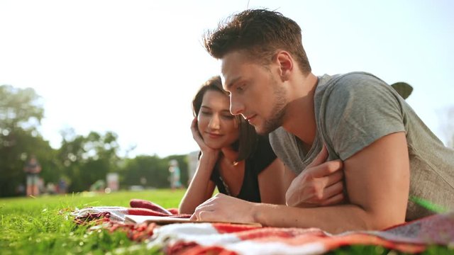 Young beautiful couple reading book, smiling, resting in park.