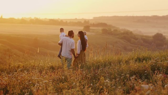 Happy family at sunset. Standing on a hill against the setting sun, holding their two children