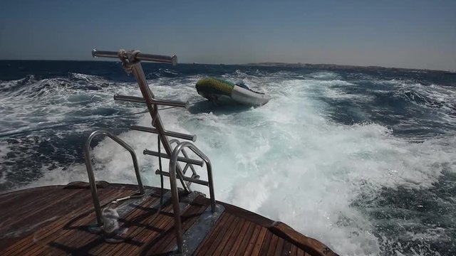 View from stern of a large luxury motor boat while sailing across tropical ocean landscape with small inflatable tender