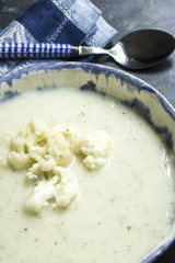 Blumenkohlsuppe mt Blumenkohlröschen in rustikaler Suppenschale mit Löffel und Serviette