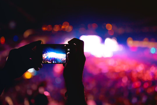 Silhouette of hands using camera phone to take pictures and videos at music concert, festival. Soft effect on photo