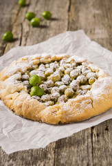 Gooseberry rustic tart on rough wooden background. Galette or crostata with fresh berries. Selective focus 